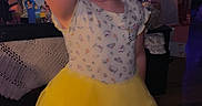 Sarah is registered to the contest to win money with this photo: child, girl, toddler, birthday, birthday_party, yellow_dress, tutu, skirt, portrait, standing, smiling, face, bow, earrings, indoor, home, decorations, gifts, television, colorful