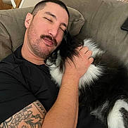 Stella is registered to the contest to win money with this photo: man, dog, couch, tattoo, sleeping, cuddling, black_and_white_dog, indoor, relaxed, pet, fur, home, resting, comfort, casual, human, animal, friendship, peaceful, closeup