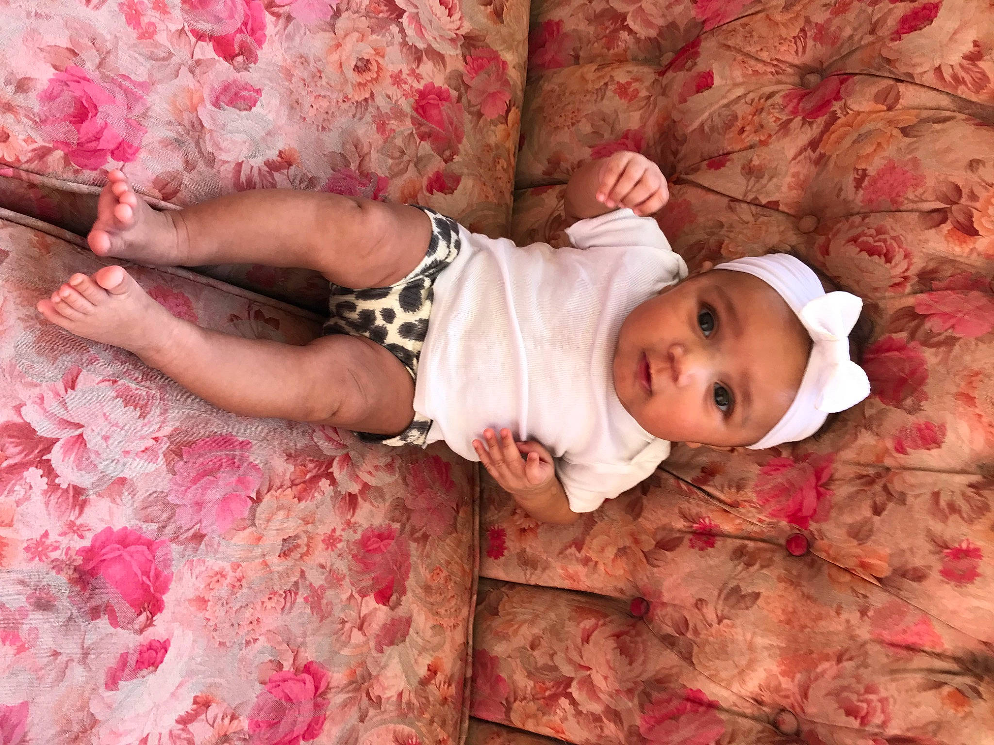 Felicity is registered to the contest to win money with this photo: arm, baby, baby_toddler_clothing, child, comfort, dress, fashion_accessory, hand, happy, headwear, human_leg, linens, pattern, person, pink, room, skin, sleeve, textile, thigh