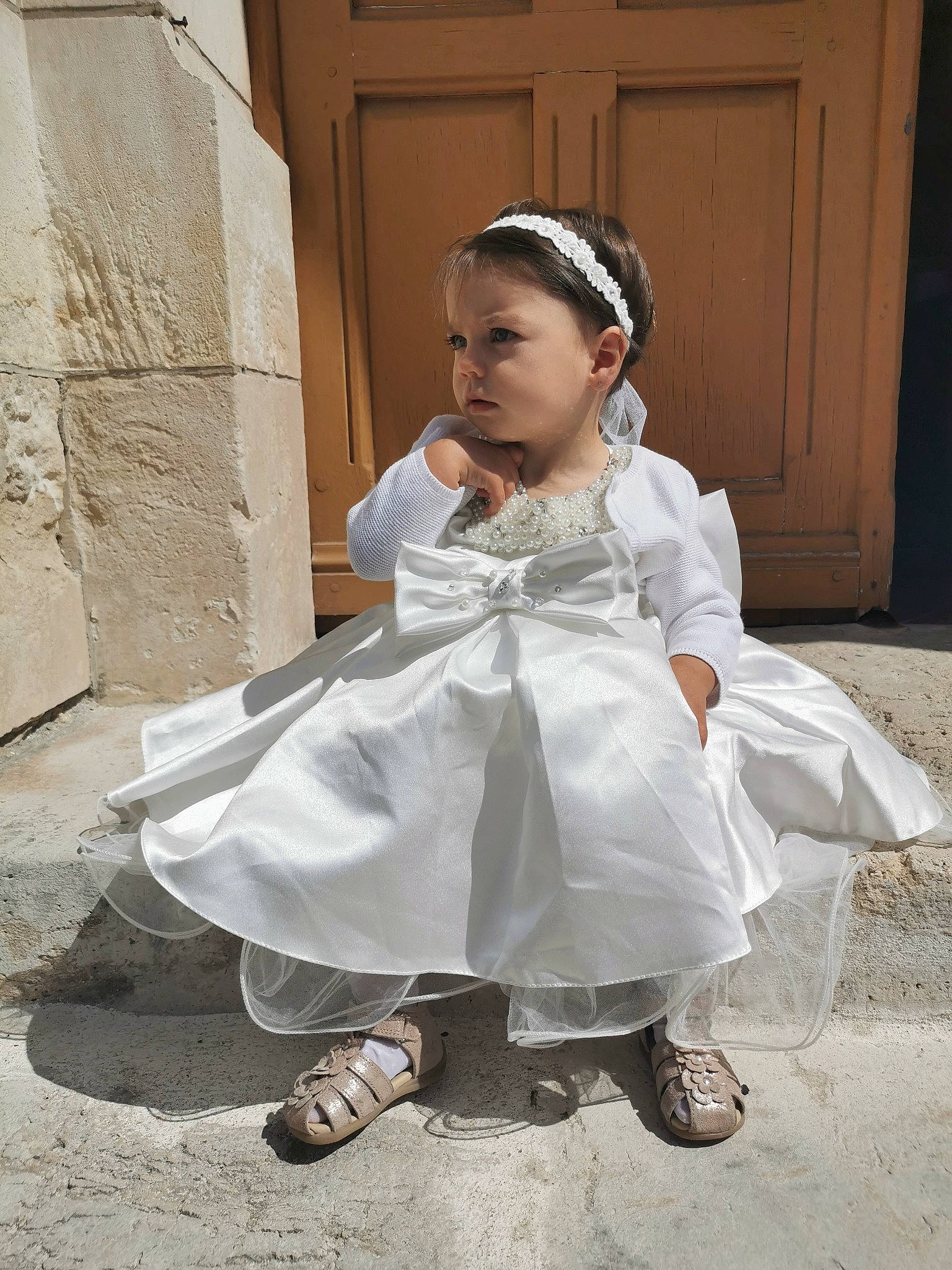 Clarence participe au concours pour gagner de l'argent avec cette photo : baby_toddler_clothing, bridal_accessory, bridal_clothing, child, door, dress, event, fashion_accessory, footwear, formal_wear, gown, hair_accessory, happy, headpiece, person, sandal, shoe, sitting, toddler, tradition