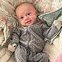 baby, infant, smile, onesie, grey_clothing, polka_dot, blanket, floral_pattern, soft_texture, cute, happy, lying_down, child, face, head, small_hands, cozy, comfort, indoor, portrait