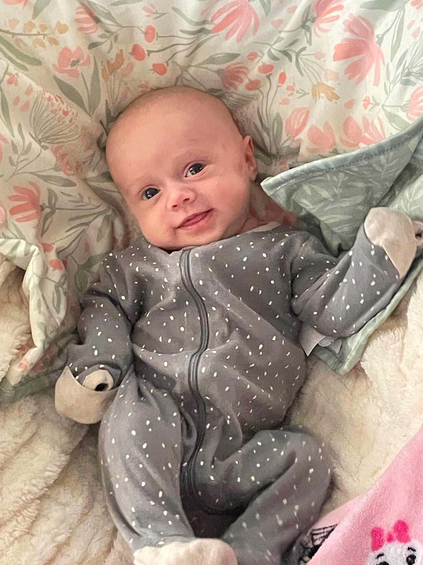 Aviana is registered to the contest to win money with this photo: baby, infant, smile, onesie, grey_clothing, polka_dot, blanket, floral_pattern, soft_texture, cute, happy, lying_down, child, face, head, small_hands, cozy, comfort, indoor, portrait