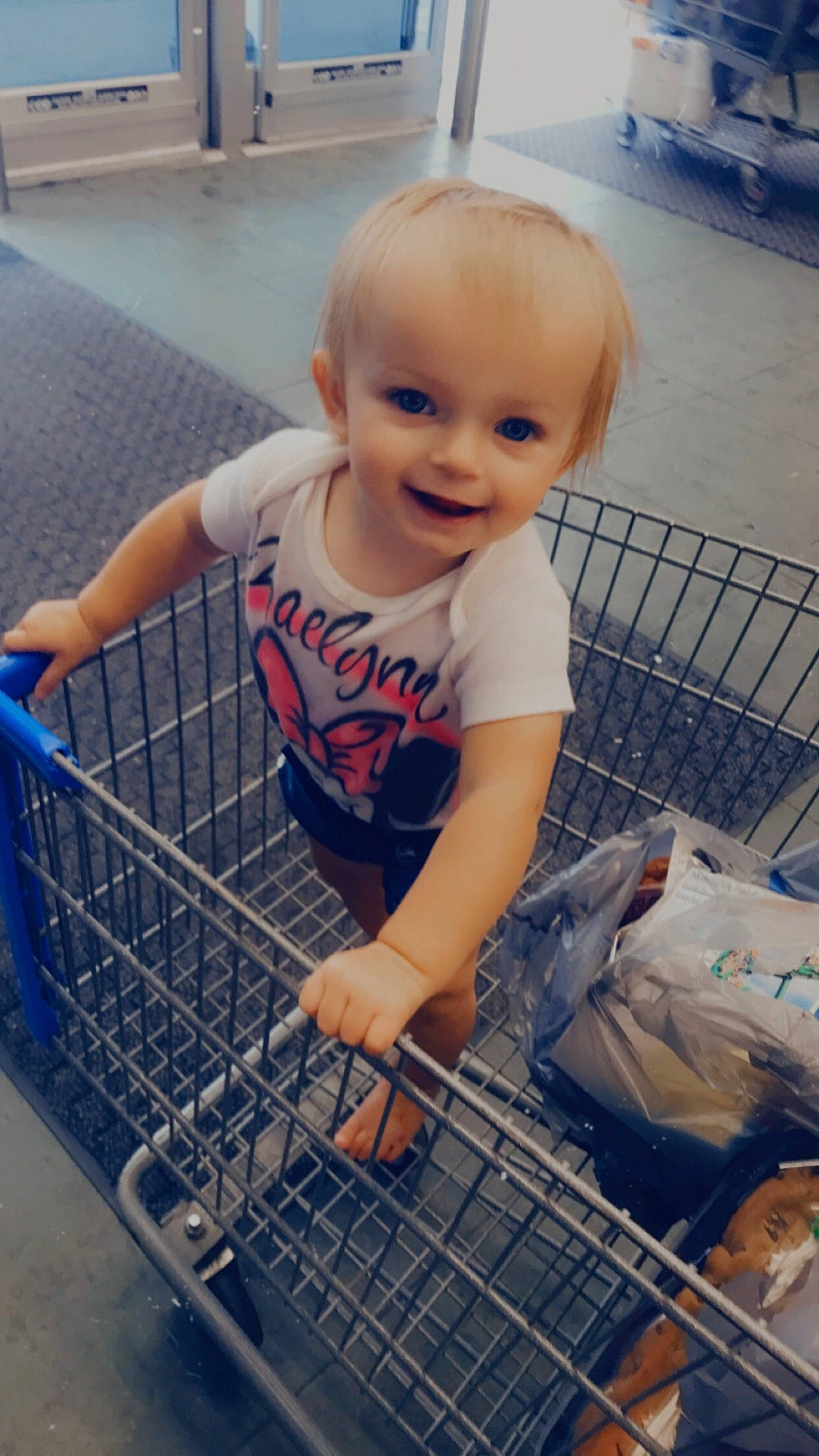 Raelynn is registered to the contest to win money with this photo: baby_toddler_clothing, beauty, blue, cart, child, flooring, fun, hand, human_leg, joy, mammal, person, photograph, product, retail, service, shopping, shopping_cart, smile, snapshot