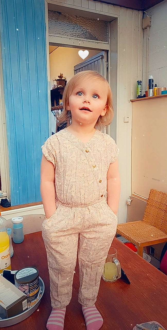 Felicia a rejoint le concours — aidez-le/la à gagner de superbes lots ! baby_toddler_clothing, child, curtain, dress, fashion_design, flooring, formal_wear, pattern, peach, person, plastic_bottle, room, sitting, sleeve, t_shirt, table, toddler, top, waist