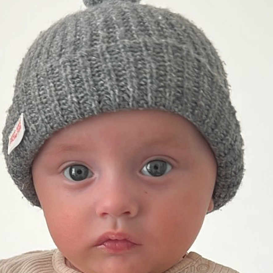 Melih a rejoint le concours — aidez-le/la à gagner de superbes lots ! baby, child, close_up, clothing, cute, expression, face, hand, hat, headwear, indoor, knit_hat, looking_at_camera, person, pom_pom, portrait, ribbed_shirt, skin, warm_clothing, young_child