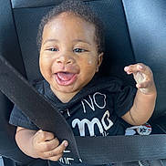 Cj joined the competition — help win amazing prizes! baby, car_seat, seatbelt, smiling, happy, child, infant, black_clothing, hand, face, curly_hair, car_interior, sitting, young_child, portrait, cute, joyful, safety, seat, cute_expression
