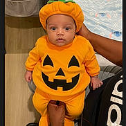Layken is registered to the contest to win money with this photo: adult, baby, blanket, child, clothing, costume, cute, expression, floor, halloween, hand, hat, holiday, indoors, infant, orange, person, portrait, pumpkin_costume, sitting