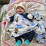 baby, infant, hat, blanket, stars, play_mat, sock, mittens, smile, face, lying_down, toy, colorful, pattern, indoor, cute, cozy, child, person, soft