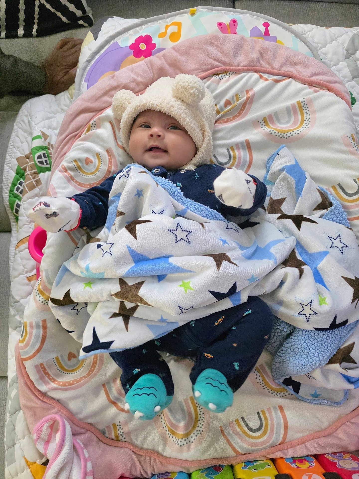 Vedanya Jain is registered to the contest to win money with this photo: baby, infant, hat, blanket, stars, play_mat, sock, mittens, smile, face, lying_down, toy, colorful, pattern, indoor, cute, cozy, child, person, soft
