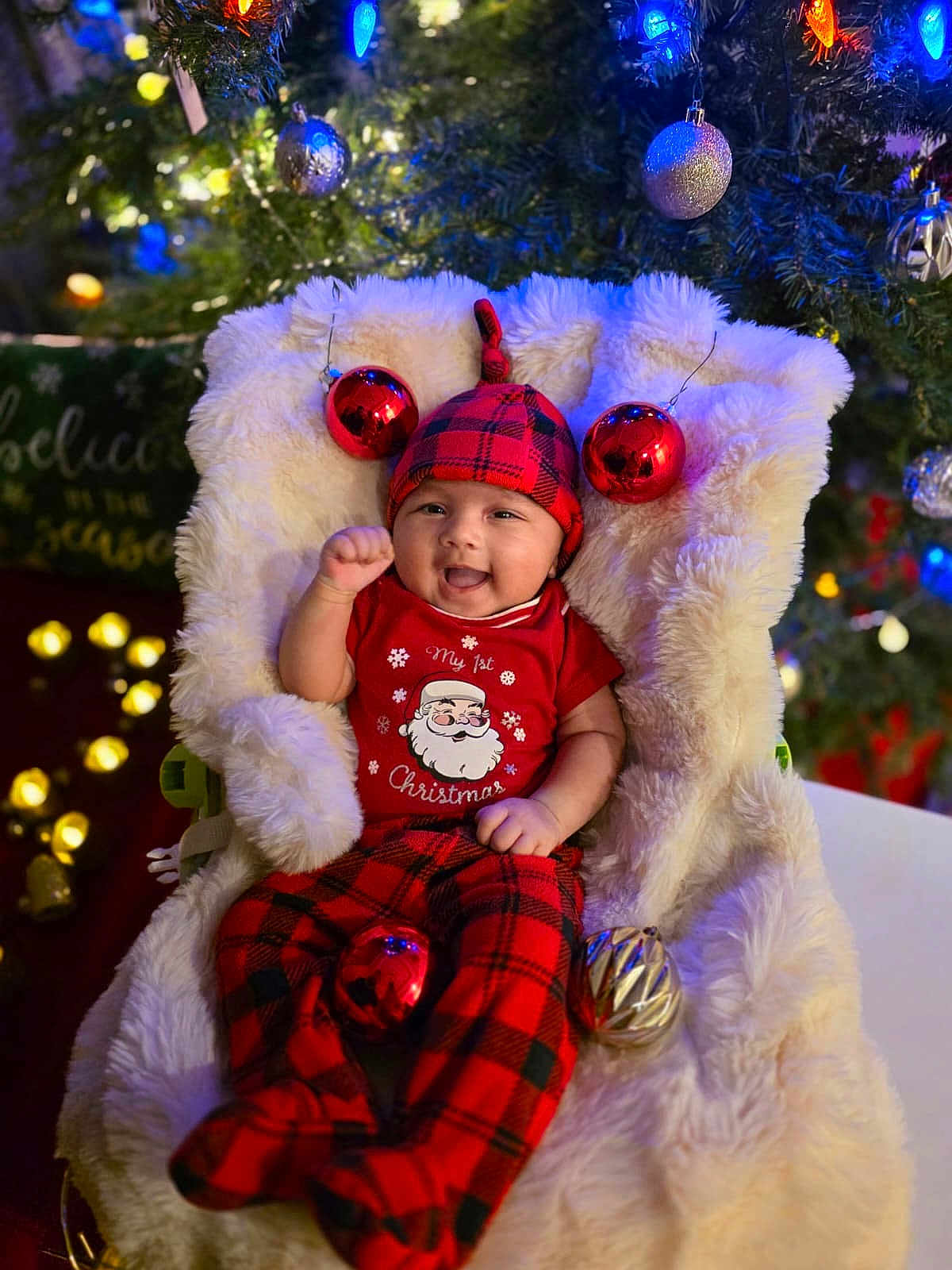 Vedanya Jain joined the competition — help win amazing prizes! baby, smiling, red_clothing, plaid_pants, christmas_tree, christmas_ornaments, holiday_lights, fluffy_blanket, festive, hat, infant, holiday, decorations, celebration, happy, indoors, seasonal, cozy, person, portrait
