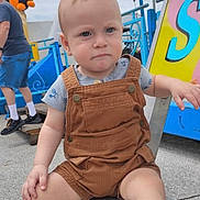 Waylon is registered to the contest to win money with this photo: toddler, child, overalls, bench, amusement_park, outdoor, person, toy, stuffed_animal, blue_shirt, shorts, shoe, hand, sky, metal, sign, adult, casual_clothing, concrete, daytime