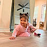 child, toddler, pink_dress, smiling, crawling, mirror, ceiling_fan, toy, minnie_mouse, wooden_floor, indoor, hair_buns, sandals, playful, home, window, door, chair, furniture, lighting