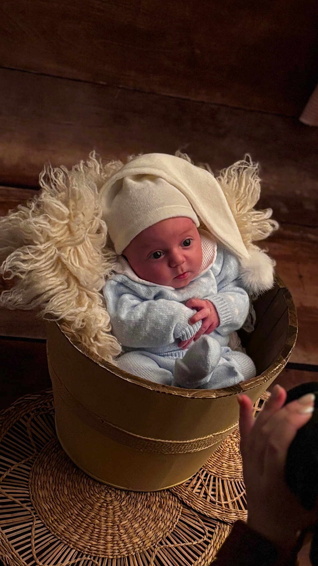 Jonas participe au concours pour gagner de l'argent avec cette photo : baby, infant, knitwear, hat, bucket, wool, yarn, cozy, cute, portrait, indoors, wood, woven_mat, hand, photography, child, newborn, soft_lighting, expression, curious