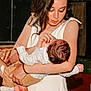 woman, baby, feeding, bottle, holding, white_dress, indoor, child, person, infant, care, love, tenderness, family, portrait, human, hair, skin, nurturing, clothing