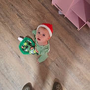 Auttumn is registered to the contest to win money with this photo: child, toddler, floor, wooden_floor, hat, red_hat, green_clothing, festive, indoor, person, footwear, crocs, cabinet, drawer, cardboard_box, toy, curious, looking_up, blur, home