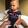 baby, child, infant, onesie, guess_logo, smartphone, bed, blanket, indoor, curious, expression, person, skin, hair, furniture, hand, sitting, technology, candid, focused