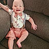 Asher is registered to the contest to win money with this photo: baby, child, smiling, couch, suspenders, shorts, floral_shirt, happy, indoor, infant, barefoot, relaxed, seated, cute, portrait, one_person, young, home, furniture, skin