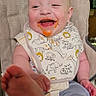 baby, high_chair, bib, messy_face, food, smiling, happy, infant, foot, clothing, indoor, cute, animal_print, child, person, playful, seat, expression, joy, light