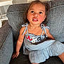 child, toddler, dress, couch, indoor, furniture, person, sitting, curly_hair, looking_up, expression, skin, smile, young_child, home, casual, cute, portrait, young_person, seated