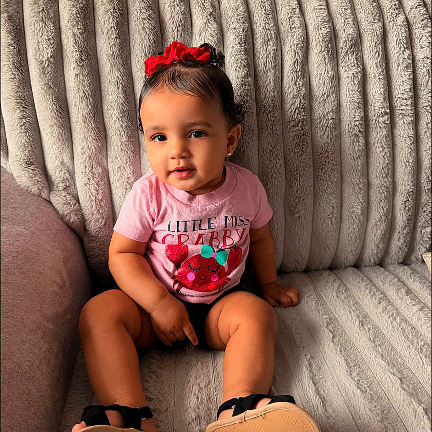 Keilani Trumbo joined the competition — help win amazing prizes! toddler, child, pink_shirt, red_bow, sitting, couch, plush, indoors, portrait, cute, smiling, face, hair, feet, shoes, window, home, cozy, young_child, person