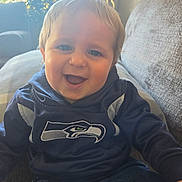 Oliver joined the competition — help win amazing prizes! baby, child, infant, smiling, happy, portrait, face, eyes, blond_hair, sitting, couch, home, indoor, lamp, window, sunlight, clothing, shirt, sports_logo, seahawks