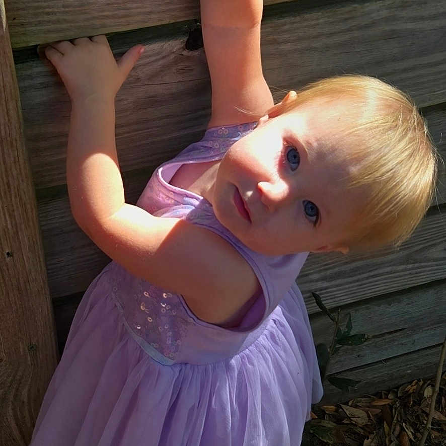 Lexi is registered to the contest to win money with this photo: blue_eyes, child, curious, dress, exploration, ground, lavender, leaves, nature, outdoor, person, playful, portrait, shadow, shoes, socks, summer, sunlight, toddler, wooden_fence