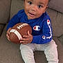 toddler, child, football, blue_sweatshirt, champion_logo, couch, sitting, white_pants, socks, indoor, cute, baby, smiling, holding_object, face, person, toy, home, playing, happy