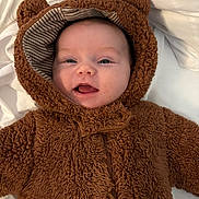 Nellie is registered to the contest to win money with this photo: baby, infant, child, cute, smiling, tongue_out, bear_costume, hood, fuzzy_clothing, soft_texture, white_blanket, portrait, closeup, happy, lying_down, warm_clothing, adorable, face, head, expressive