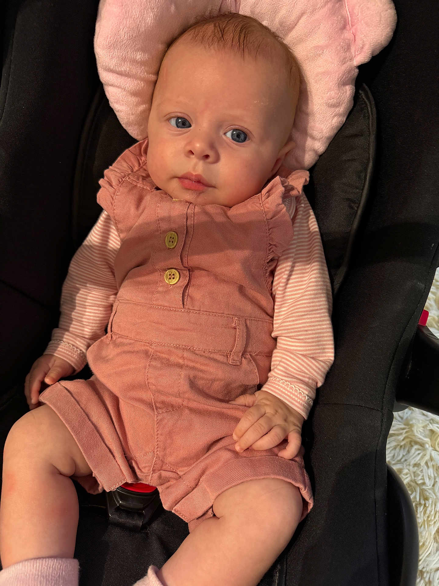 Paula participe au concours pour gagner de l'argent avec cette photo : baby, infant, car_seat, pink_clothing, romper, striped_shirt, blue_eyes, soft_cushion, hand, legs, cute, child, indoors, portrait, seatbelt, clothing, person, skin, head, expression