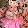 baby, child, pink_dress, bow, headband, rainbow_blanket, colorful, cute, infant, sitting, portrait, indoors, soft_toys, chubby_cheeks, clothing, patterned, happy, person, young_child, baby_girl