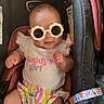 Logan is registered to the contest to win money with this photo: baby, child, sunglasses, car_seat, clothing, infant, smile, person, cute, colorful, striped, bow, white_shirt, pink, yellow, accessory, seatbelt, toy, happy, portrait