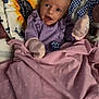 baby, blanket, polka_dot, purple_clothing, mittens, star_toy, moon_toy, sunflower_pattern, cushion, infant, face, expression, soft_toys, bed, sleeping_area, child, portrait, indoors, cute, comfort