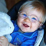 Don Carlu a rejoint le concours — aidez-le/la à gagner de superbes lots ! baby, child, glasses, blue_eyes, smiling, teddy_bear, plush_toy, blue_shirt, seated, cushion, happy, portrait, cute, infant, closeup, indoor, person, soft_toy, clothing, accessory