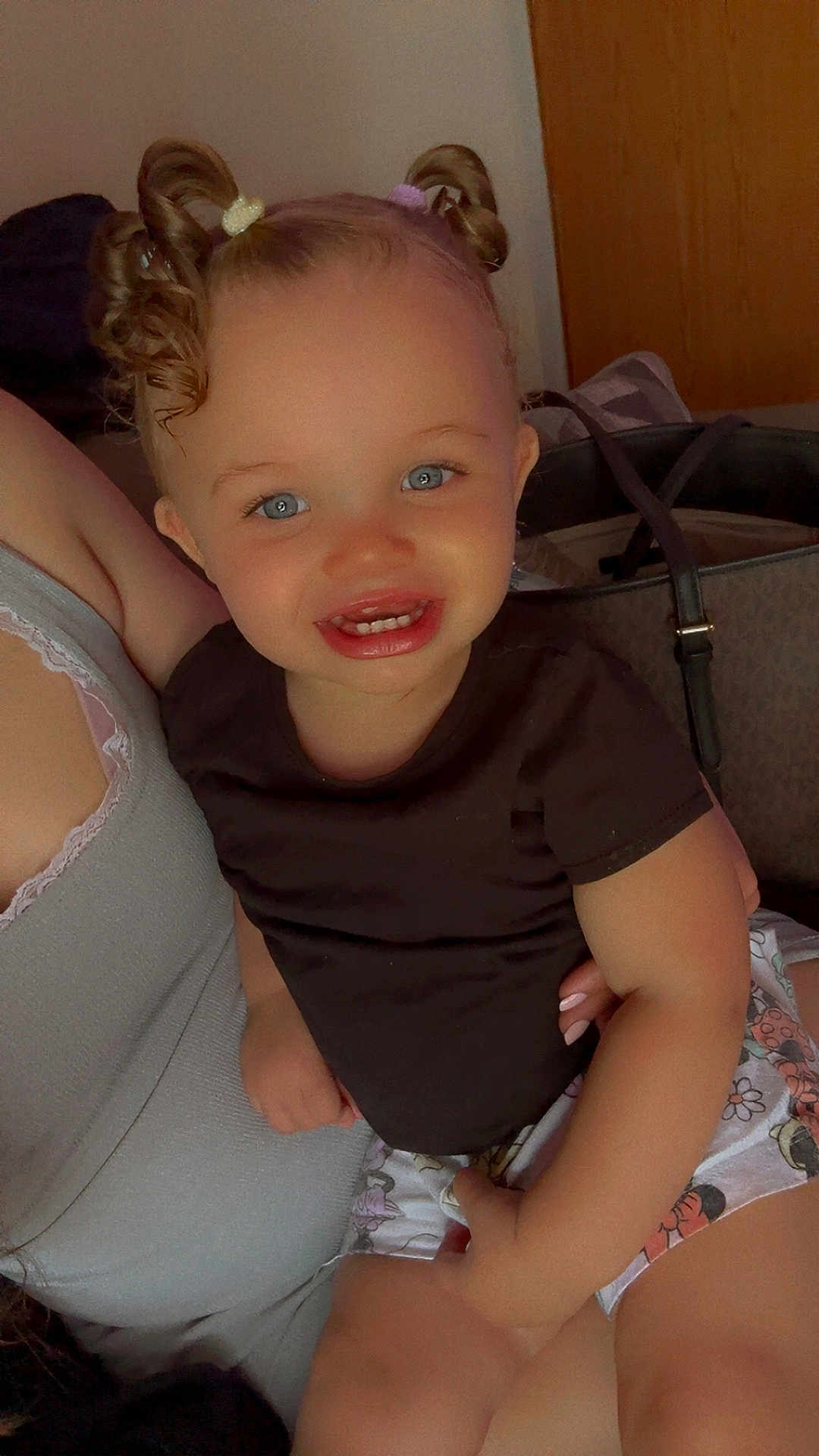 Elyana joined the competition — help win amazing prizes! toddler, child, smiling, curly_hair, pigtails, black_shirt, floral_shorts, sitting, lap, person, indoor, happy, cute, face, blue_eyes, skin, hand, bag, door, portrait
