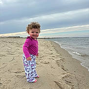 Elyana joined the competition — help win amazing prizes! toddler, child, beach, sand, water, ocean, sky, cloudy, curly_hair, smile, standing, clothing, pajamas, hello_kitty, footwear, nature, outdoor, shoreline, happy, portrait