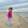 toddler, child, beach, sand, water, ocean, sky, cloudy, curly_hair, smile, standing, clothing, pajamas, hello_kitty, footwear, nature, outdoor, shoreline, happy, portrait
