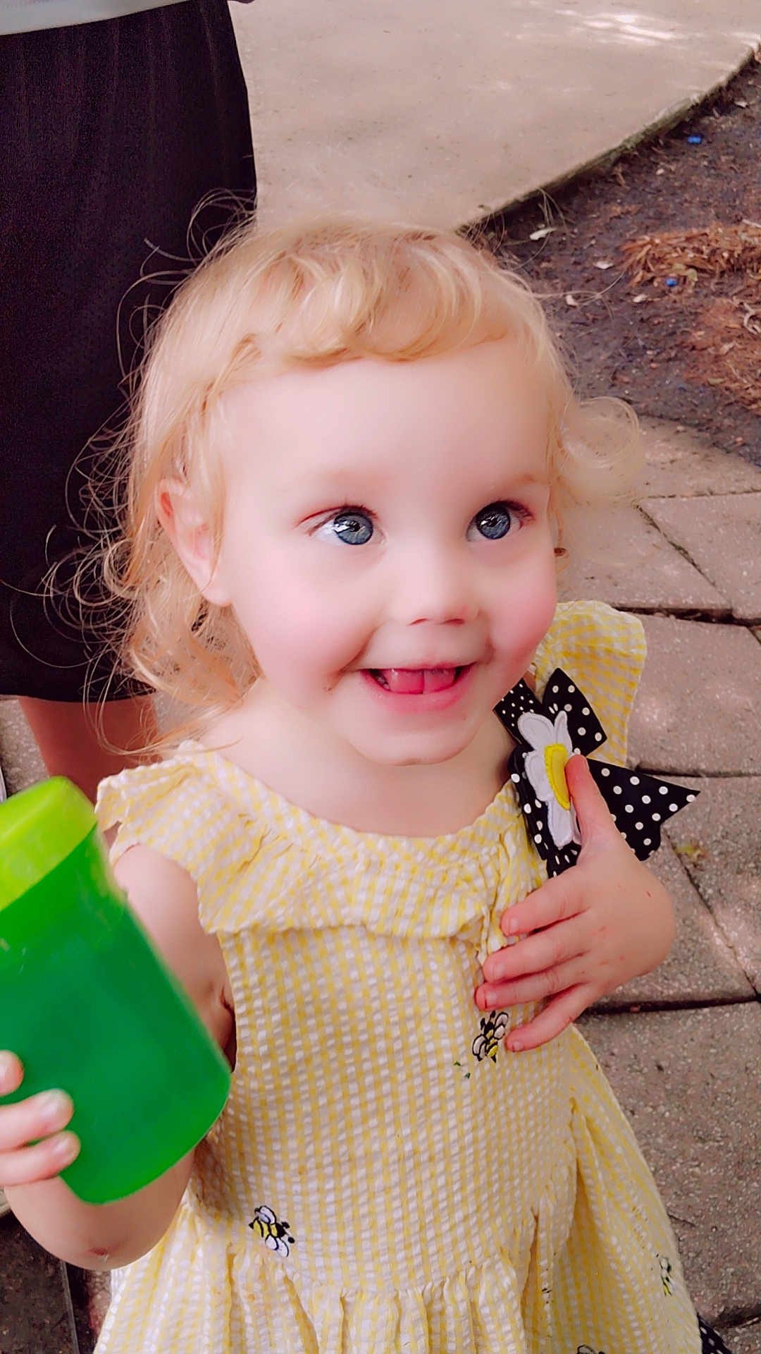 Celestia joined the competition — help win amazing prizes! toddler, child, smiling, blonde_hair, blue_eyes, yellow_dress, bee_embroidery, polka_dot_bow, daisy, green_cup, hand, outdoor, pavement, soil, leaves, person, clothing, happy, curly_hair, portrait