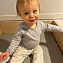 baby, barefoot, bench, blue_eyes, child, clothing, cute, face, gray_shirt, happy, indoor, light_pants, person, portrait, sitting, skin, smile, toddler, wooden_furniture, young_child