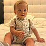 baby, bed, blue_eyes, bowtie, child, clothing, curious, cute, headboard, indoor, person, portrait, shirt, shoes, shorts, sitting, suspenders, toddler, white_bedspread, young