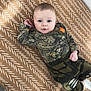Tripp joined the competition — help win amazing prizes! baby, child, infant, camo_clothing, blue_eyes, blanket, patterned_blanket, lying_down, indoor, soft_light, curious_expression, small_hand, casual_wear, cute, comfort, face, person, young_child, head, socks