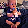 baby, infant, child, teething_toy, blue_clothing, bed, pillow, blanket, plush_toy, cow_print, indoor, person, cute, sitting, hands, feet, face, eyes, expression, soft_lighting