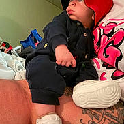 Grayson joined the competition — help win amazing prizes! baby, child, red_hood, navy_blue_outfit, white_shoes, tattoo, arm, indoor, person, curious_expression, seated, clothing, footwear, hand, casual, wall, fabric, colorful, looking_away, skin