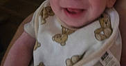 Grayson is registered to the contest to win money with this photo: baby, smile, bib, teddy_bear, infant, person, cute, happy, child, arm, hand, skin, clothing, indoor, portrait, young, face, holding, expression, closeup