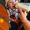 baby, bottle, milk, feeding, high_chair, child, hat, bucket_hat, tattoo, hand, table, wood, blue_eyes, smiling, indoor, clothing, person, infant, cute, dining
