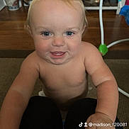 Peanut is registered to the contest to win money with this photo: baby, child, indoor, smiling, face, blue_eyes, skin, arm, hand, floor, carpet, toy, furniture, person, knees, playful, expression, closeup, portrait, light