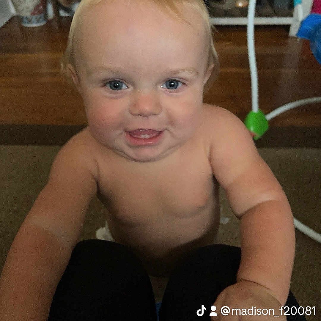 Peanut is registered to the contest to win money with this photo: baby, child, indoor, smiling, face, blue_eyes, skin, arm, hand, floor, carpet, toy, furniture, person, knees, playful, expression, closeup, portrait, light