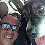 black_dog, car_interior, casual, close_up, companion, dog, glasses, happy, indoors, man, pet, portrait, reflection, seat, seatbelt, selfie, smile, tongue_out, white_markings, window