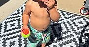 Zayden is registered to the contest to win money with this photo: toddler, child, hat, bucket_hat, sunglasses, red_sunglasses, tennis_ball, barefoot, shorts, patterned_rug, outdoor, patio, sunny, shadow, concrete, door, hose, summer, playful, person