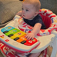 Jensen is registered to the contest to win money with this photo: baby, walker, toy_piano, colorful, indoor, carpet, child, infant, seated, hand, foot, clothing, face, person, play, curious, furniture, living_room, plastic, soft_lighting