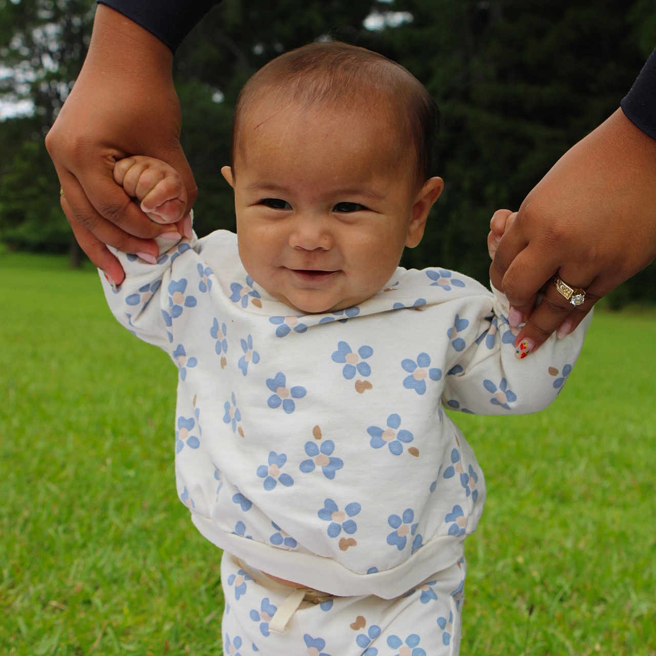 Suliana is registered to the contest to win money with this photo: baby, child, infant, grass, outdoor, nature, hands, support, walking, clothing, floral_pattern, smile, person, blanket, greenery, cute, toddler, playing, family, holding_hands